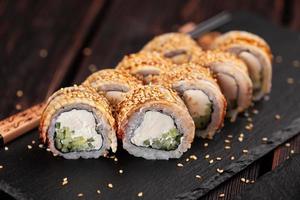 cocina japonesa - rollo de sushi con pepino y queso crema cubierto con un primer plano de anguila en una pizarra negra foto