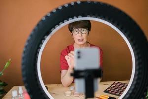 Middle-aged woman talking on cosmetics with makeup eye shadows and blush palette and brushes while recording her video. Mature female making video for her blog on cosmetics photo