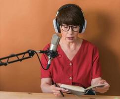 Portrait of mature woman wearing headphones and talking at online radio station - podcast and broadcast concept photo