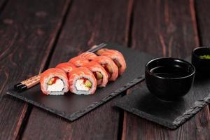 rollo de sushi maguro con salmón, aguacate y tobiko, queso filadelfia en primer plano de pizarra negra. menú de sushi comida japonesa. foto