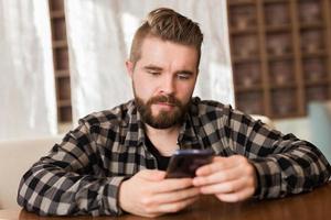 Man holding modern digital smartphone device and chatting in social networks. Guy sending message on cellular while sitting at table in cafe photo