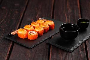 Sushi roll with salmon, avocado and tobiko caviar served on black board close-up - Japanese asian food photo