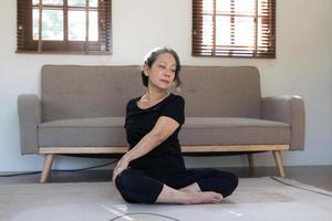 Healthy and happy 60s retired Asian woman in workout clothes practicing yoga in her living room. photo