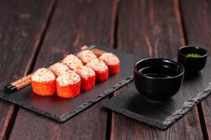 Sushi roll with mayonnaise sauce and red tobiko caviar served on black board and soy sauce. photo