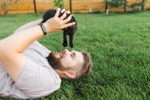 hombre con gatito acostado y jugando en la hierba - amistad amor animales y concepto de dueño de mascota foto