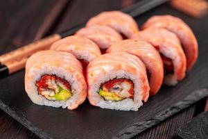 Sushi roll maguro with tuna, smoked eel, avocado and tobiko on black board close-up. Sushi menu. Japanese food.