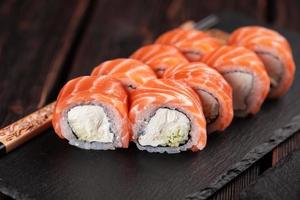 sushi roll philadelphia con salmón y pepino y queso crema en primer plano de fondo negro. menú de sushi concepto de comida japonesa foto