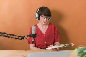 Mature woman making podcast recording for her online show. Attractive business woman using headphones front of microphone for a radio broadcast photo