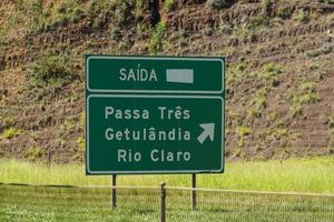 cartel amarillo de la carretera que indica la dirección de la ciudad en una carretera en brasil que señala una curva hacia adelante en una carretera foto