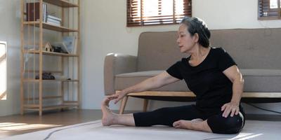 Healthy and happy 60s retired Asian woman in workout clothes practicing yoga in her living room. photo