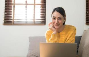 retrato de una joven mujer feliz sentada en el sofá y trabajando en un proyecto, viendo una película en una laptop, estudiando, blogueando, descansando y charlando en línea. foto