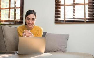 retrato de una joven mujer feliz sentada en el sofá y trabajando en un proyecto, viendo una película en una laptop, estudiando, blogueando, descansando y charlando en línea. foto