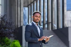 joven hombre de negocios afroamericano en traje de negocios formal de pie trabajando con tableta foto