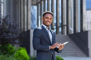 joven hombre de negocios afroamericano en traje de negocios formal de pie trabajando con tableta foto