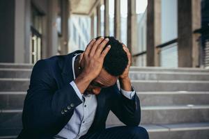 trabajador de oficina masculino cansado después del trabajo, afroamericano tiene dolor de cabeza severo, sentado foto