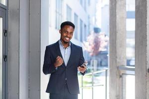 salió de un hombre de negocios afroamericano celebrando un logro mirando un teléfono inteligente foto