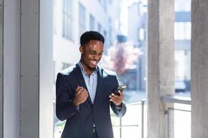 Exited African American Businessman Celebrating Achievement looking at Smartphone photo