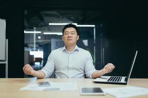 un descanso en el trabajo. apuesto joven hombre de negocios asiático meditando en el lugar de trabajo en la oficina foto