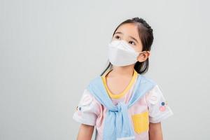 niña asiática con mascarilla respiratoria para proteger el brote de coronavirus y apuntando con la mano al fondo en blanco, nuevo virus covid-19 foto