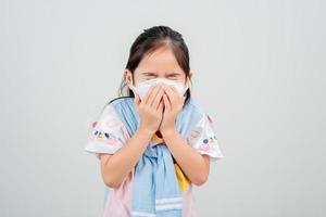 niña asiática con mascarilla respiratoria para proteger el brote de coronavirus y apuntando con la mano al fondo en blanco, nuevo virus covid-19 foto