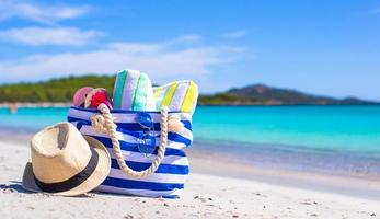 Blue bag, straw hat, flip flops and towel on white beach photo