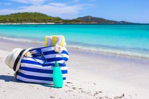 Stripe bag, straw hat, sunblock and towel on beach photo