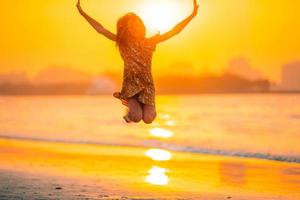 Adorable happy little girl on white beach at sunset. photo