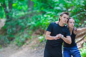 Young active couple looking at smart watch heart rate monitor having break while running at forest photo