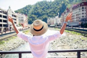 chica feliz con sombrero en el terraplén de un río de montaña en una ciudad europea. foto