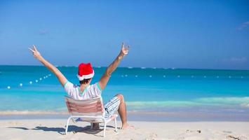 vista trasera del joven con sombrero de santa durante las vacaciones en la playa foto