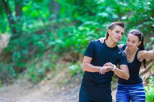 Young active couple looking at smart watch heart rate monitor having break while running at forest photo