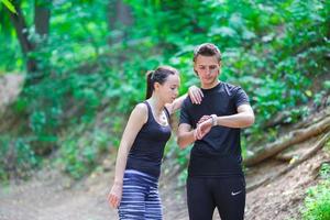 Young active couple looking at smart watch heart rate monitor having break while running at forest photo