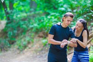 Young active couple looking at smart watch heart rate monitor having break while running at forest photo