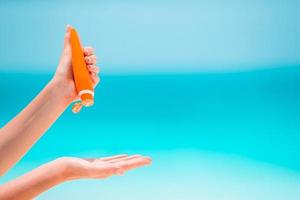 Beautiful young woman holding a suncream lying on tropical beach photo