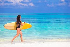 Happy shapely surf woman at white beach with yellow surfboard photo