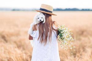 niño feliz en campo de trigo. hermosa chica vestida de blanco con un sombrero de paja con trigo maduro en las manos foto