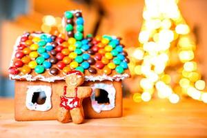 Homemade Christmas Gingerbread House on a table. Christmas tree lights in the background photo