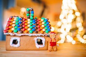 Homemade Christmas Gingerbread House on a table. Christmas tree lights in the background photo