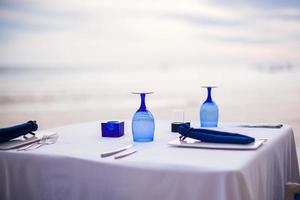 Summer empty open air table set for dinner on white beach photo