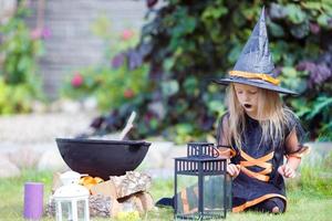 Adorable little girl wearing witch costume casting a spell on Halloween. Trick or treat. photo