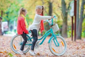 Adorable little girls riding a bike at beautiful autumn day outdoors photo