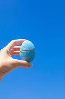 hermoso y brillante huevo de pascua en la mano sobre el fondo del cielo azul foto