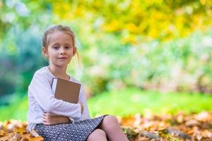 Adorable little clever girl with book in beautiful autumn dau outdoors photo