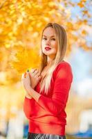 Fall concept - beautiful woman drinking coffee in autumn park under fall foliage photo