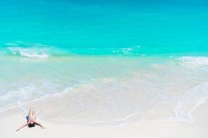 Top view of young beautiful girl lying on the beach at shallow tropical water on the seashore photo