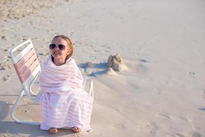 adorable niñita con gafas de sol cubierta con una toalla en la playa tropical foto