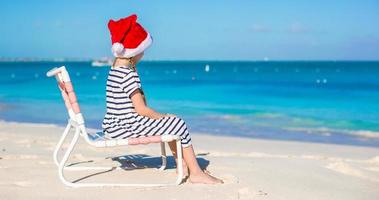 Little adorable girl in Santa hat at tropical white beach photo