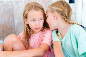 Funny little girls in an outdoor cafe on sunny summer day. Kids whisper while waiting the food photo