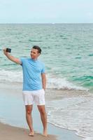 Young man taking selfie by smartphone while walking on the beach photo