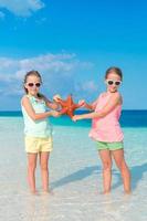 adorables niñas con estrellas de mar en una playa blanca y vacía foto